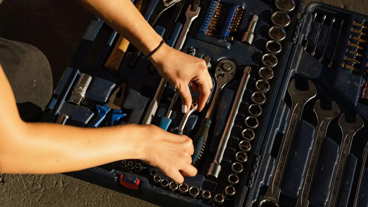 Vue de dessus de mains qui rangent des clés et des douilles dans une boîte à outils bleue