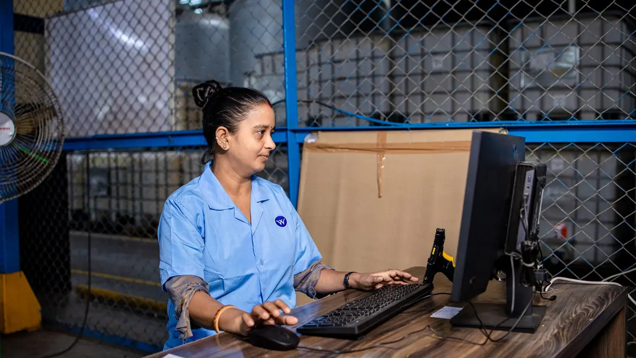 Une employée en blouse bleue saisit des données sur un poste informatique dans un entrepôt d'usine