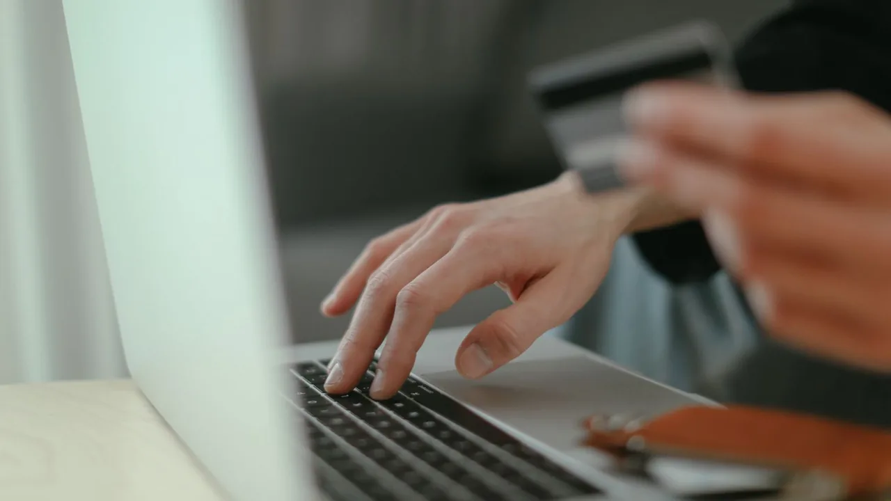 Une main tient une carte bancaire tandis que l'autre tape sur le clavier d'un ordinateur portable