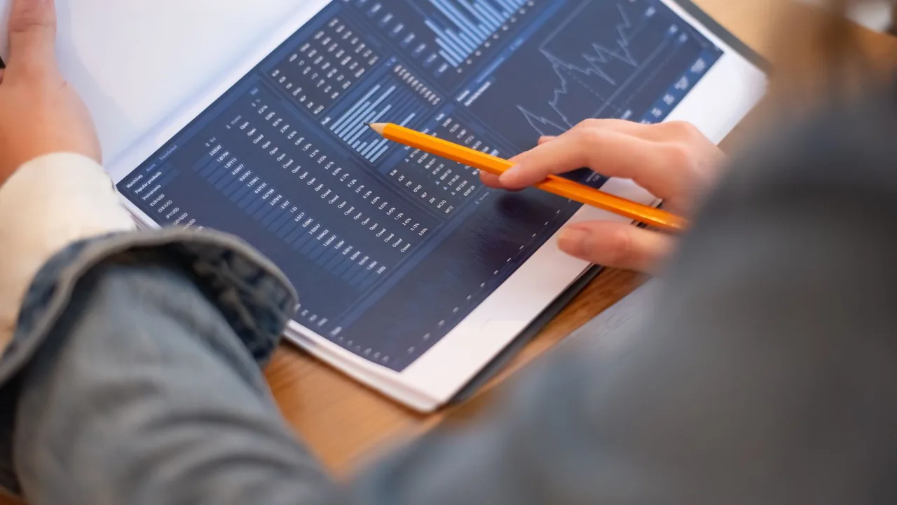 Des mains pointent un crayon sur un tableau de chiffres et de graphiques imprimé