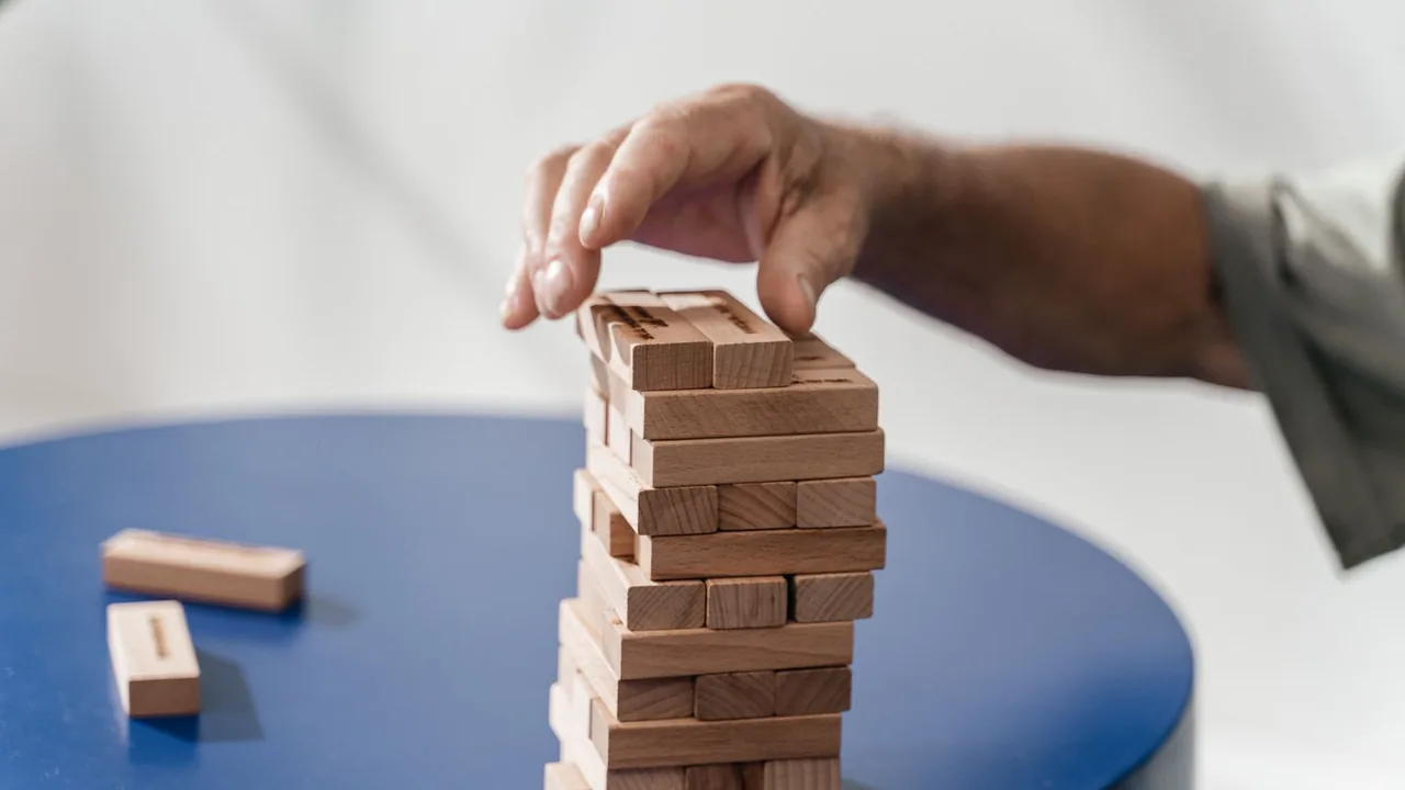 Main posant un bloc en bois au sommet d'une tour de blocs empilés, sur une table ronde bleue