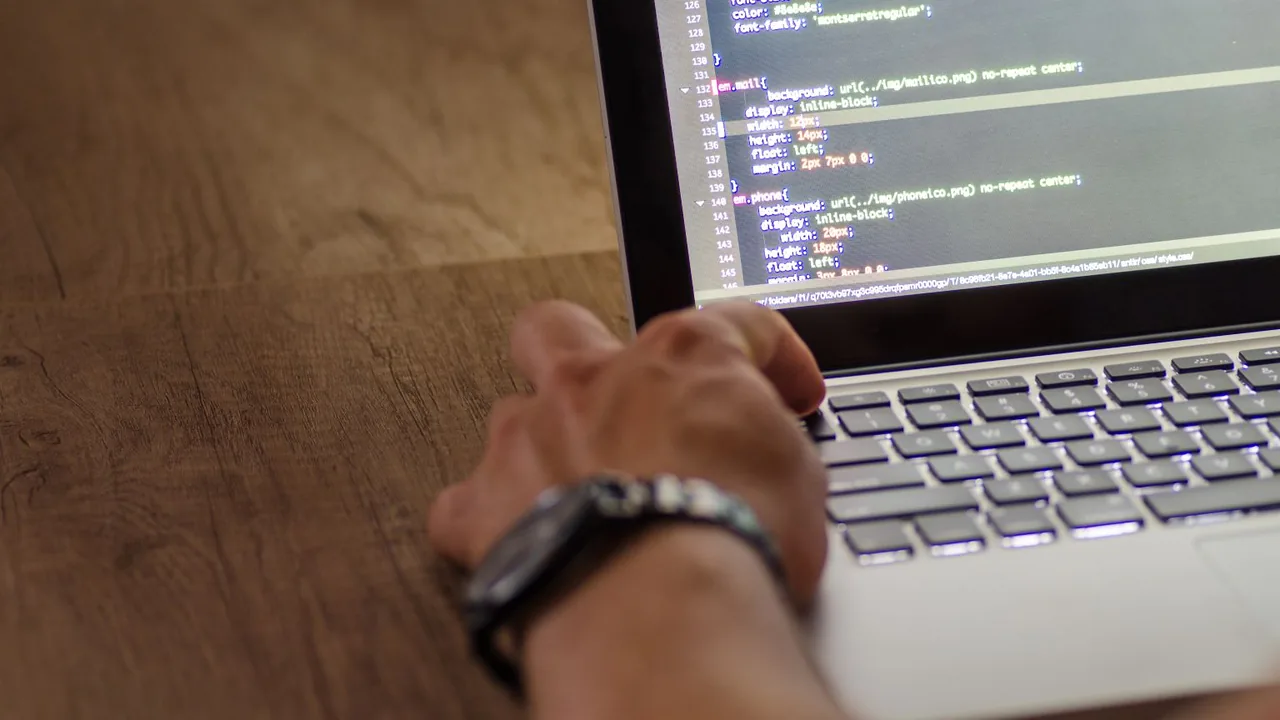 Gros plan sur une main qui tape sur le clavier d'un ordinateur portable posé sur un bureau en bois