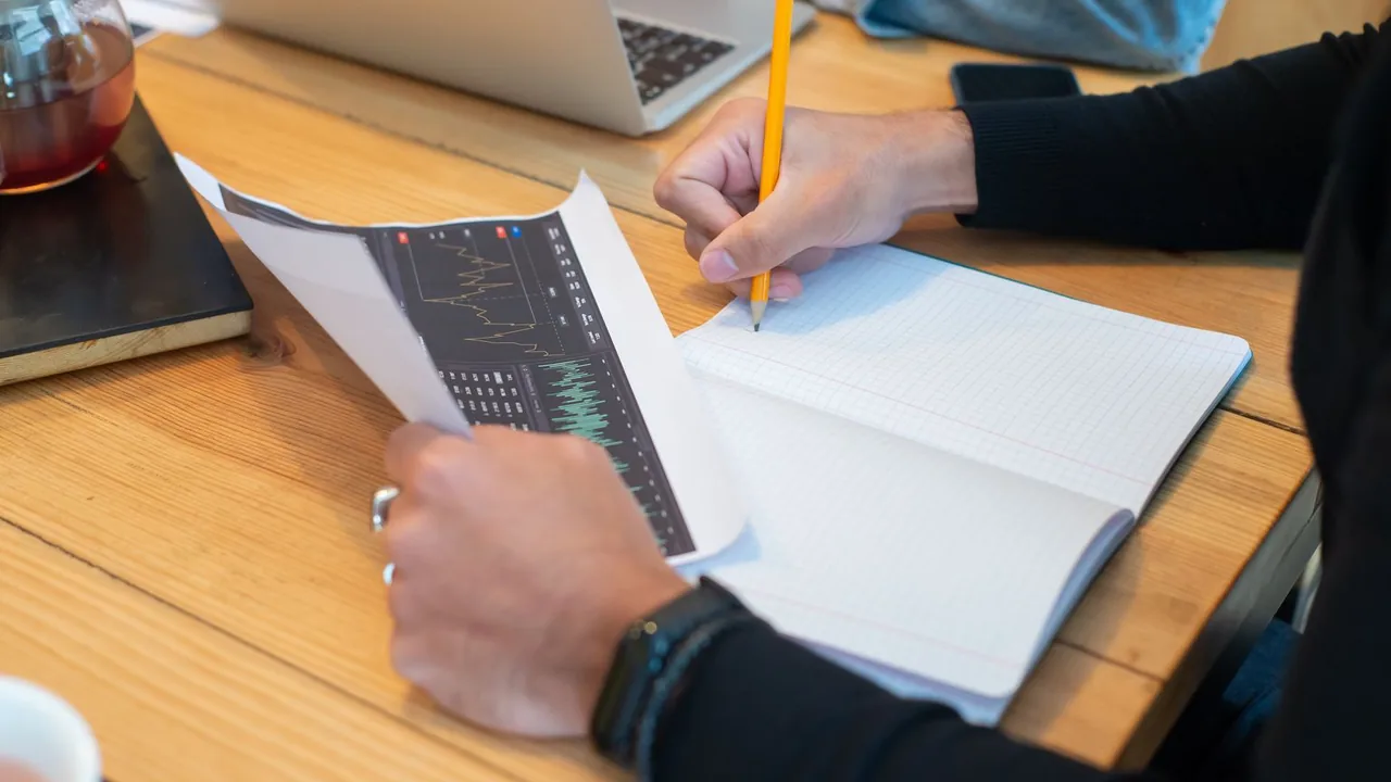 Des mains écrivent dans un carnet à côté de graphiques imprimés sur un bureau en bois