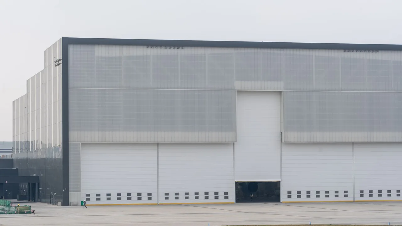 Grand bâtiment industriel gris aux portes de hangar fermées, sous un ciel voilé