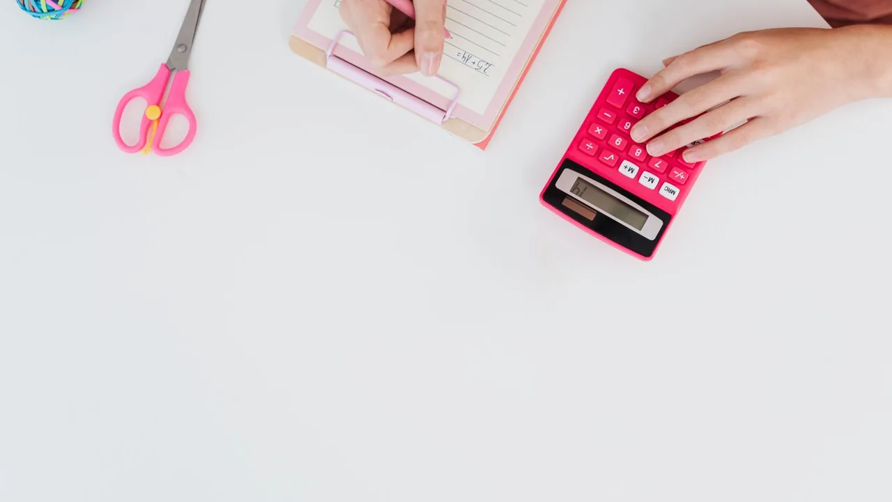 Mains sur une calculatrice rose et un bloc-notes, sur un bureau blanc, avec une paire de ciseaux roses