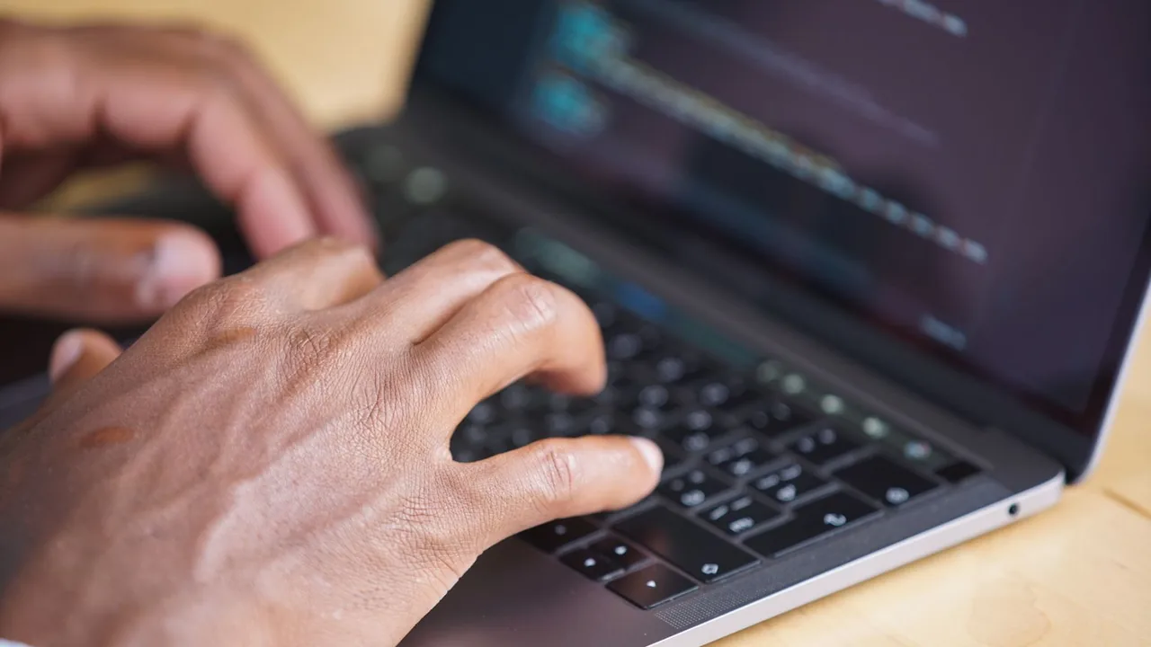 Gros plan sur des mains qui tapent sur le clavier d'un ordinateur portable posé sur un bureau en bois