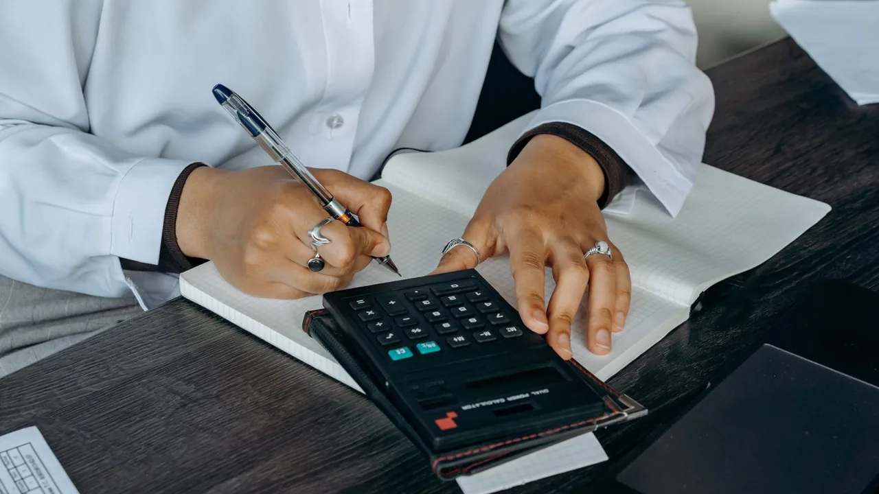 Une professionnelle prend des notes dans un carnet, une calculatrice posée sur un bureau en bois