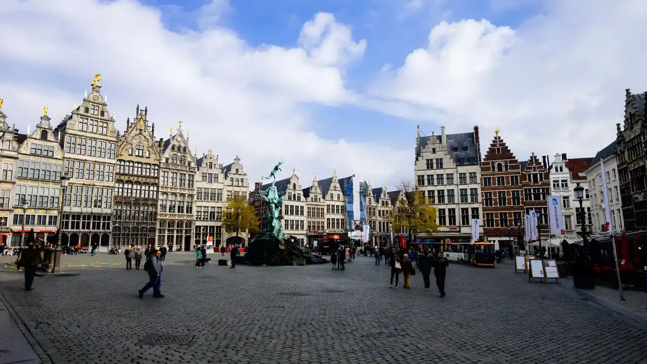 Une place pavée d'Anvers bordée de façades historiques, avec la fontaine Brabo et des passants