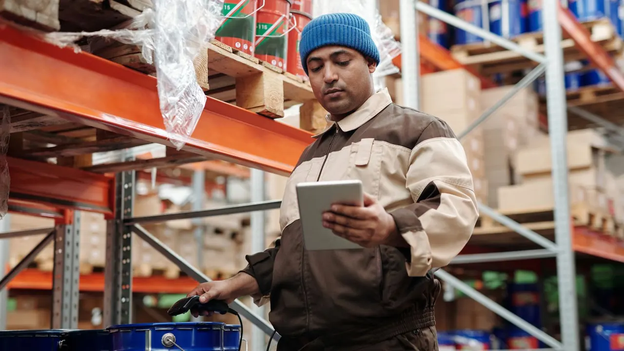Un employé en bonnet bleu consulte une tablette entre des rayonnages d'entrepôt