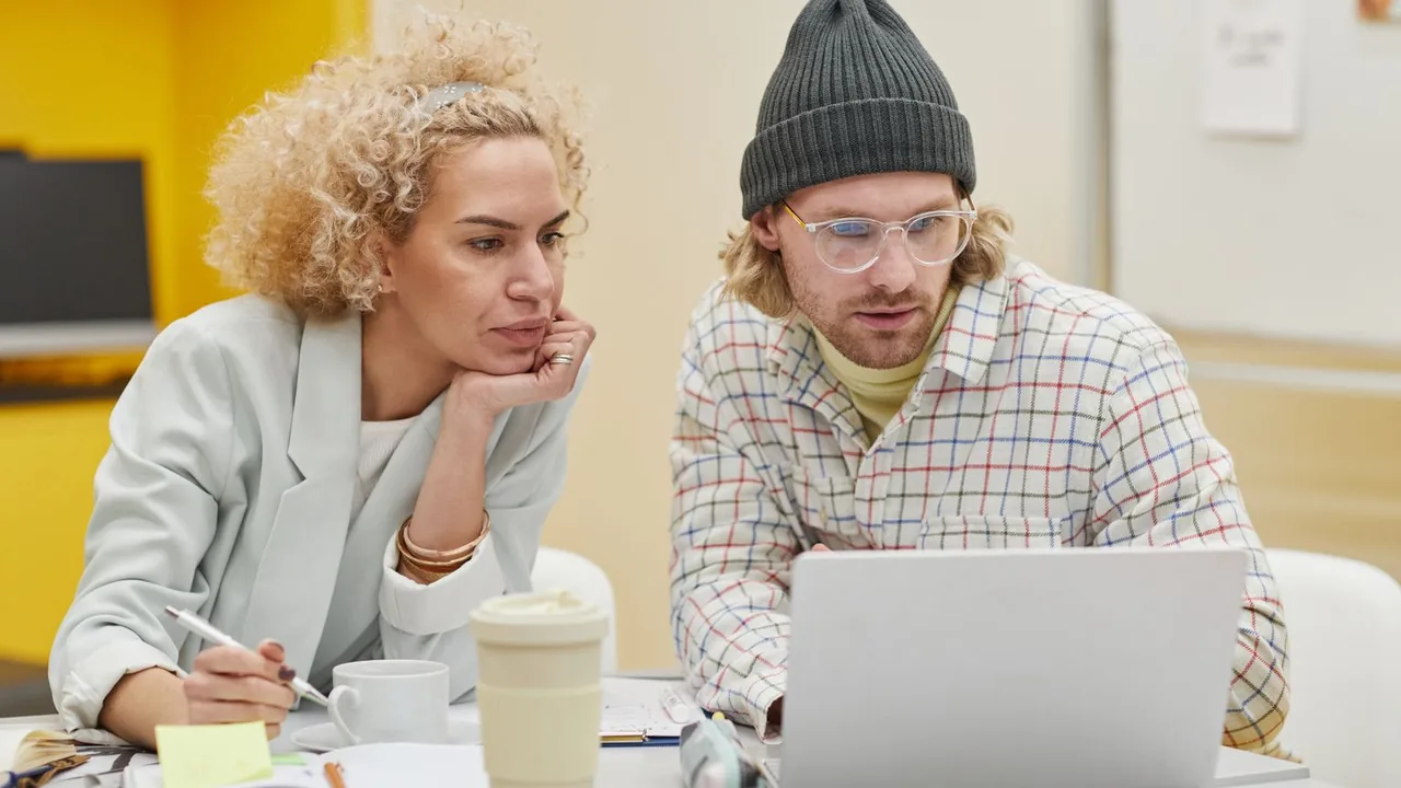 Deux collègues discutant d'un projet devant un ordinateur portable, carnet de notes sur la table
