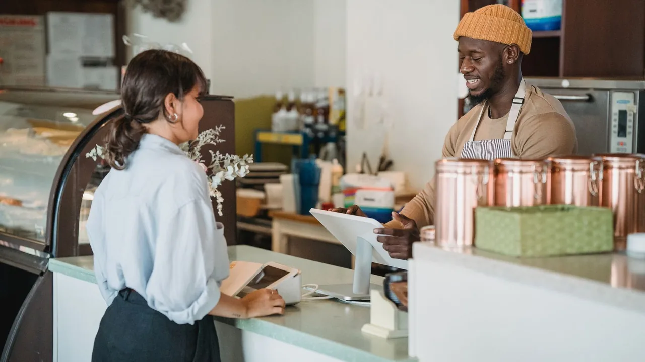 Un barista et une cliente discutent au comptoir devant la caisse tactile du café