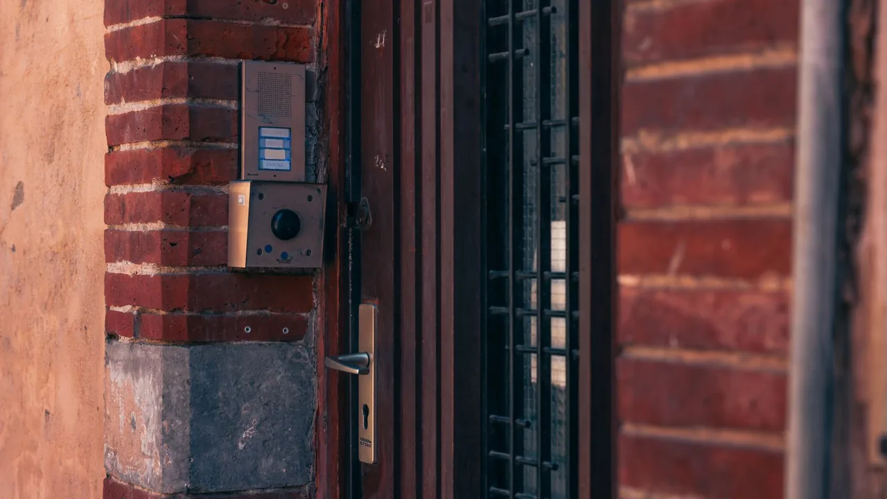 Un interphone et une caméra fixés sur le mur de briques rouges d'une porte d'entrée