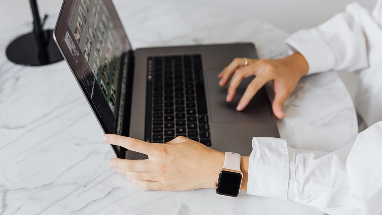 Une femme en chemise blanche utilise un ordinateur portable ouvert sur une table en marbre, une montre connectée au poignet