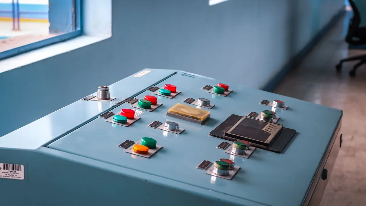 Gros plan sur un pupitre de commande industriel bleu-vert avec boutons rouges et verts