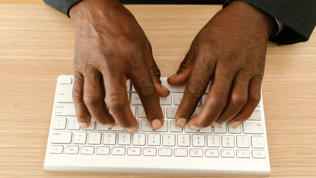 Gros plan sur des mains qui tapent sur un clavier blanc sans fil, sur un bureau en bois clair