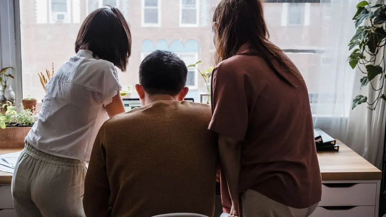 Trois collègues vus de dos, penchés ensemble sur un bureau devant une fenêtre