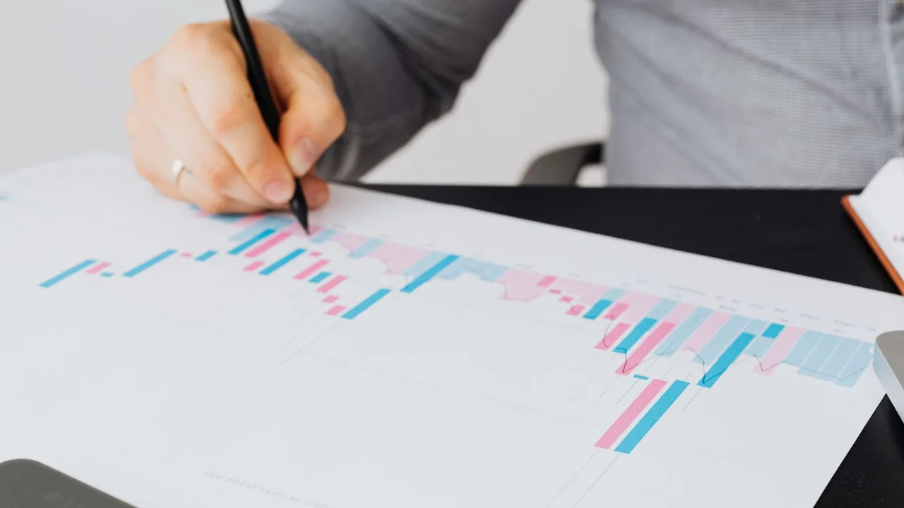 Une main annote au stylo un graphique en barres roses et bleues imprimé