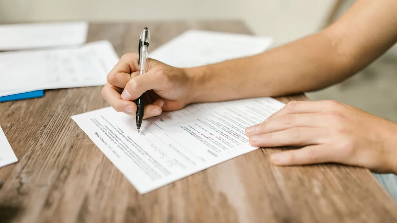 Une main remplit un document avec un stylo sur une table en bois