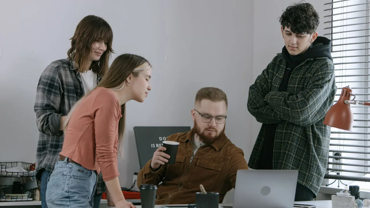 Quatre collègues réunis autour d'un ordinateur portable dans un bureau clair