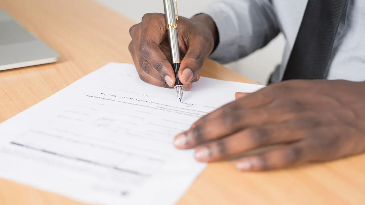 Une main signe un document avec un stylo-plume sur un bureau clair