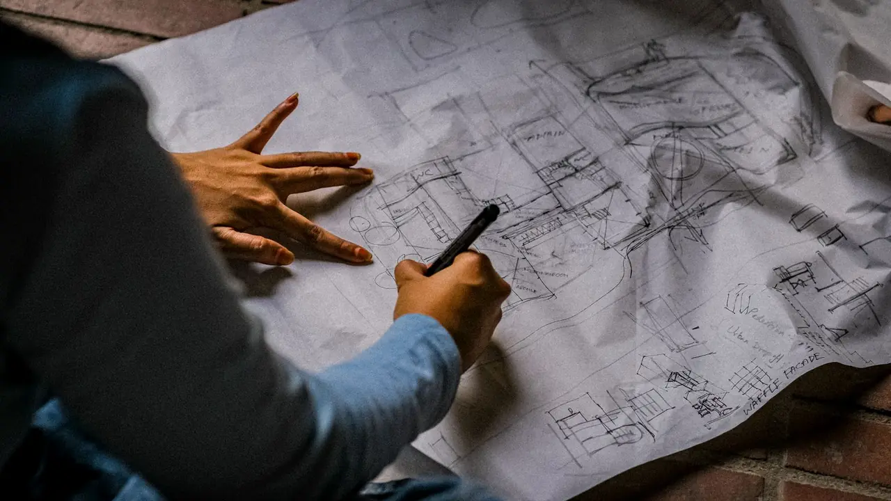 Des mains dessinent au feutre un plan d'aménagement sur un grand papier calque