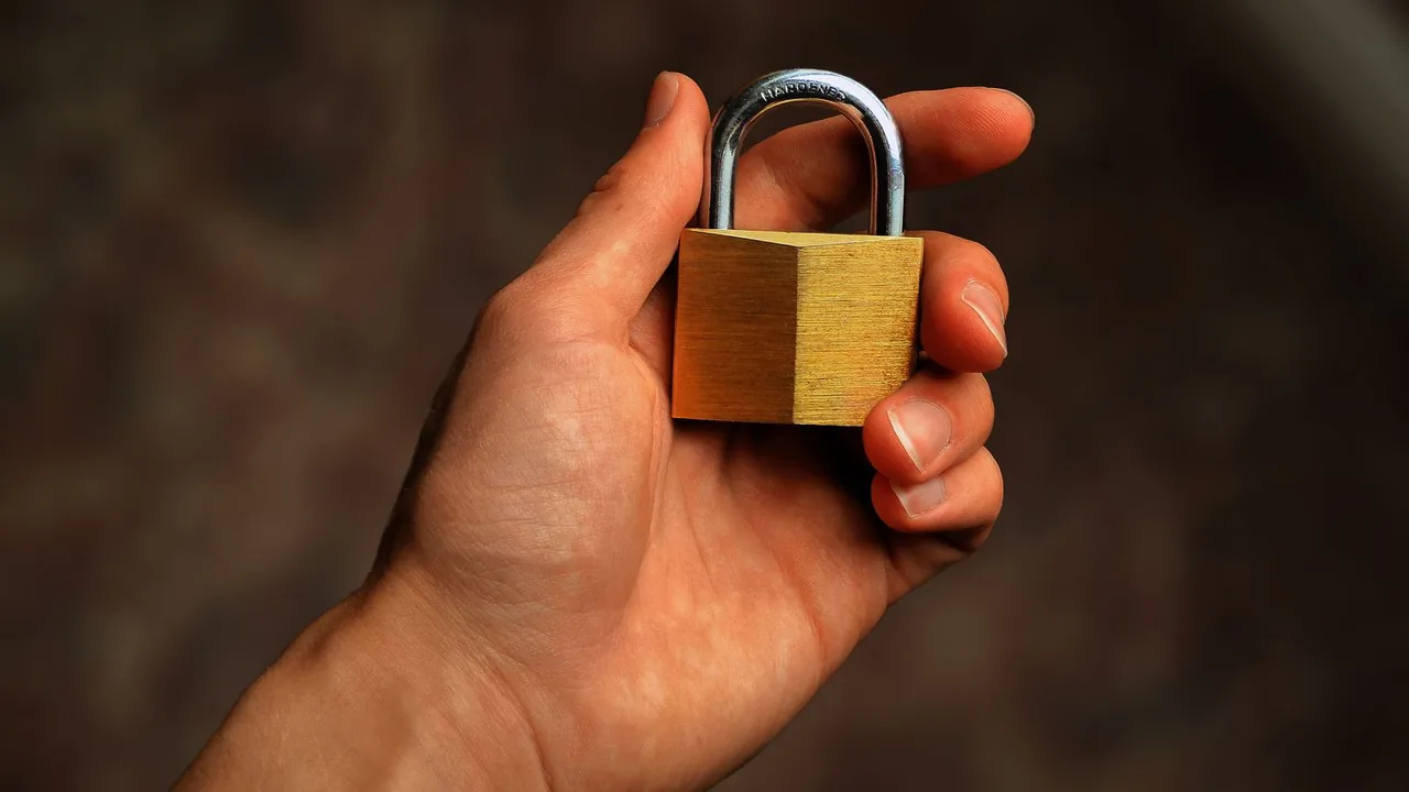 Une main tient un cadenas en laiton sur un fond sombre flou