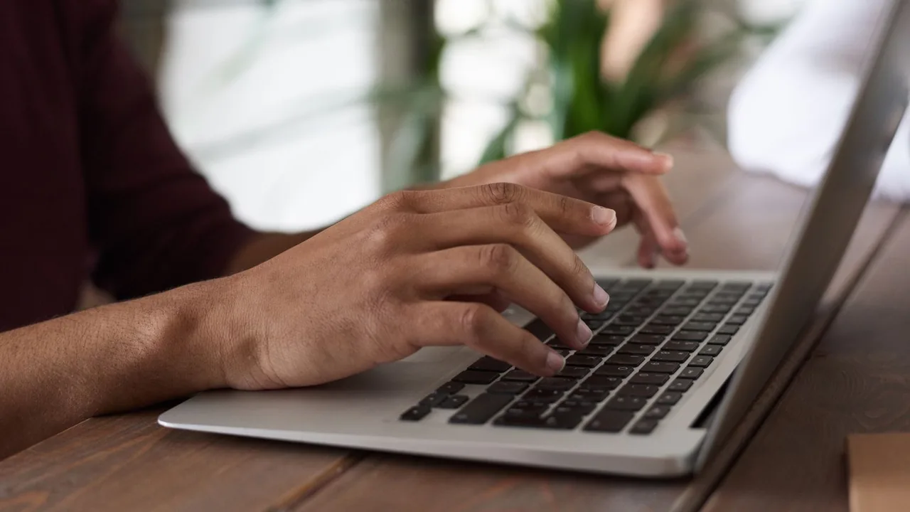 Les mains d'une personne tapent sur le clavier d'un ordinateur portable posé sur une table en bois