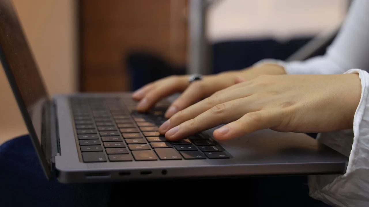 Des mains tapent sur le clavier d'un ordinateur portable posé sur un bureau