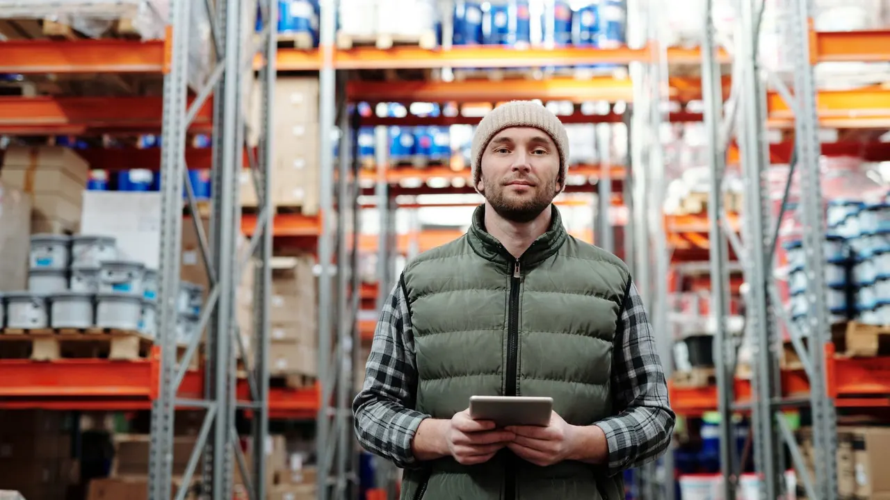 Un employé en gilet et bonnet tient une tablette entre des rayonnages de stockage dans un entrepôt