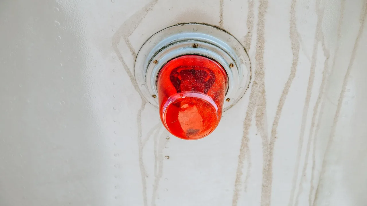 Gyrophare rouge fixé à un mur blanc taché, signal d'alerte