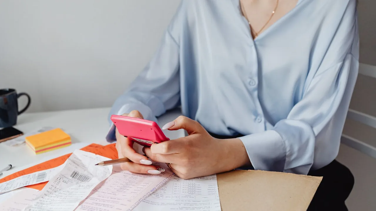 Femme calculant des dépenses avec une calculatrice rose, entourée de factures et de reçus