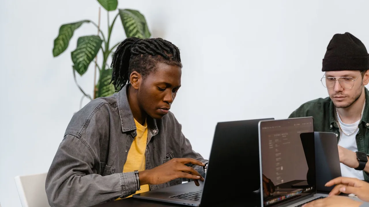 Deux jeunes collègues concentrés sur leurs ordinateurs portables, plante verte derrière eux