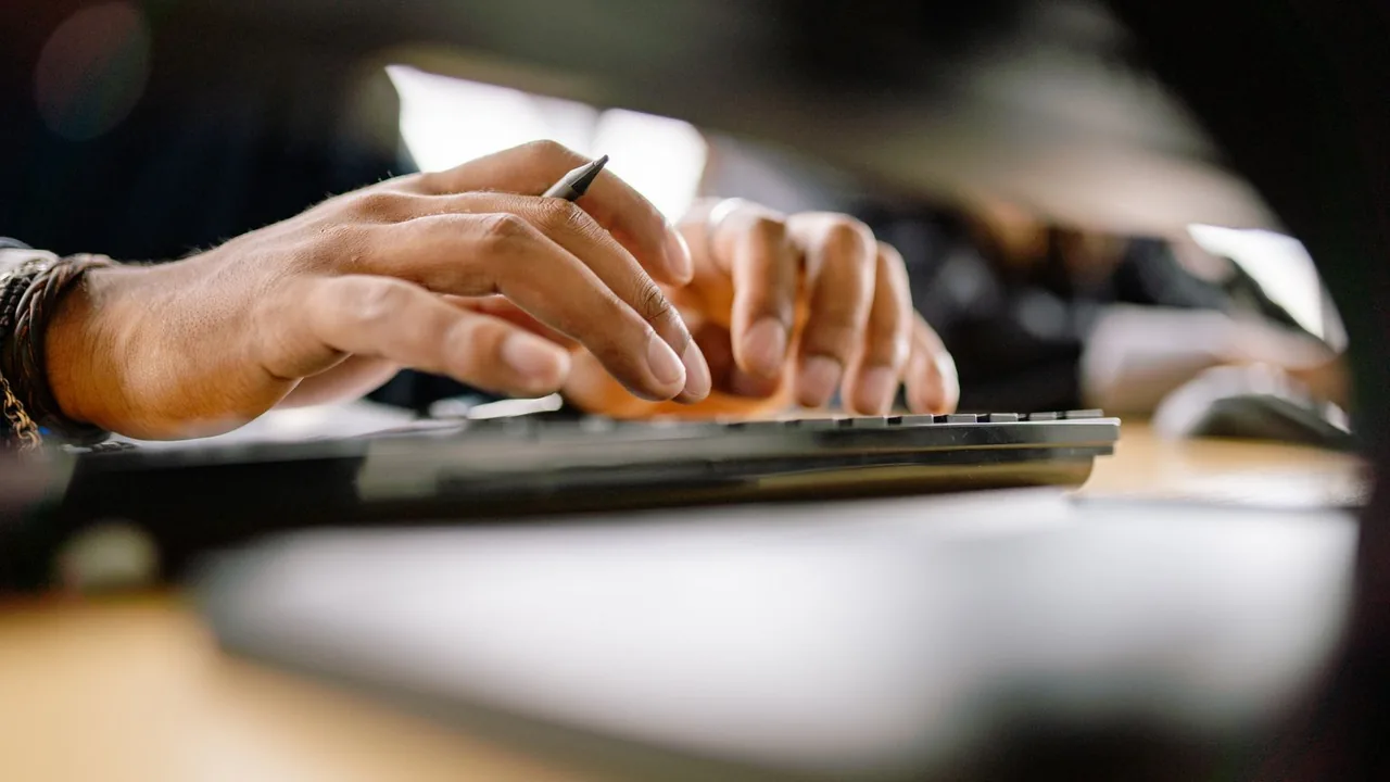 Gros plan sur une main tenant un stylo au-dessus d'un clavier, sur un bureau en bois