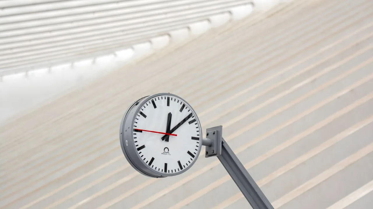 Horloge de gare ronde fixée à un mât devant un plafond blanc strié