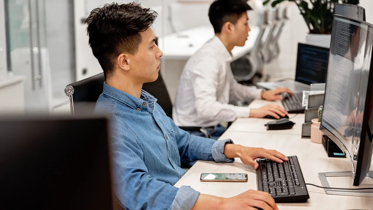 Deux jeunes développeurs travaillent côte à côte devant leurs écrans dans un bureau lumineux