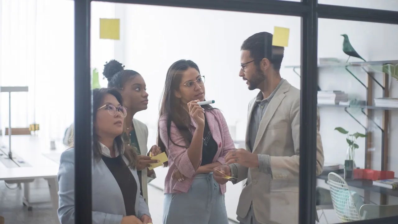 Quatre collègues échangent derrière une paroi vitrée sur laquelle sont collés des post-it