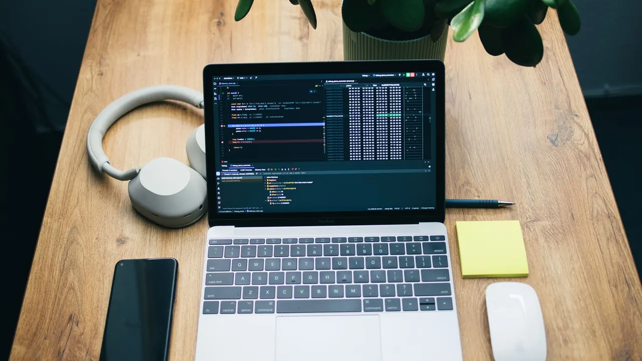 Vue de dessus d'un bureau en bois avec un ordinateur portable ouvert, un casque, un téléphone et un bloc-notes