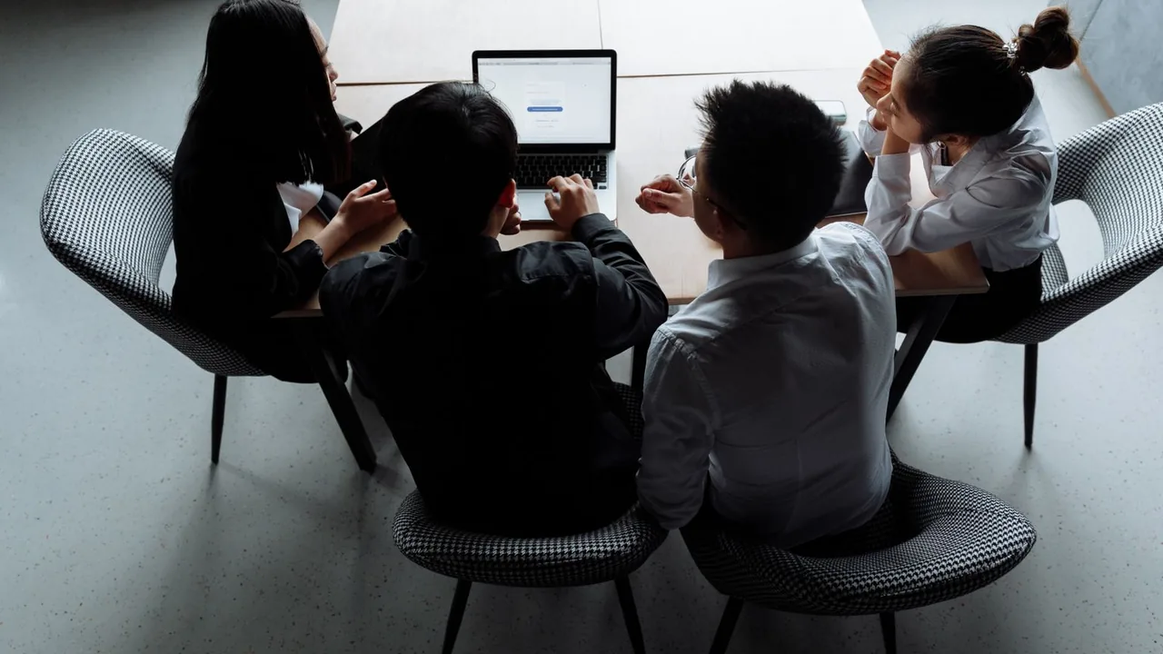 Vue de dessus de quatre collègues assis autour d'une table, penchés sur un ordinateur portable