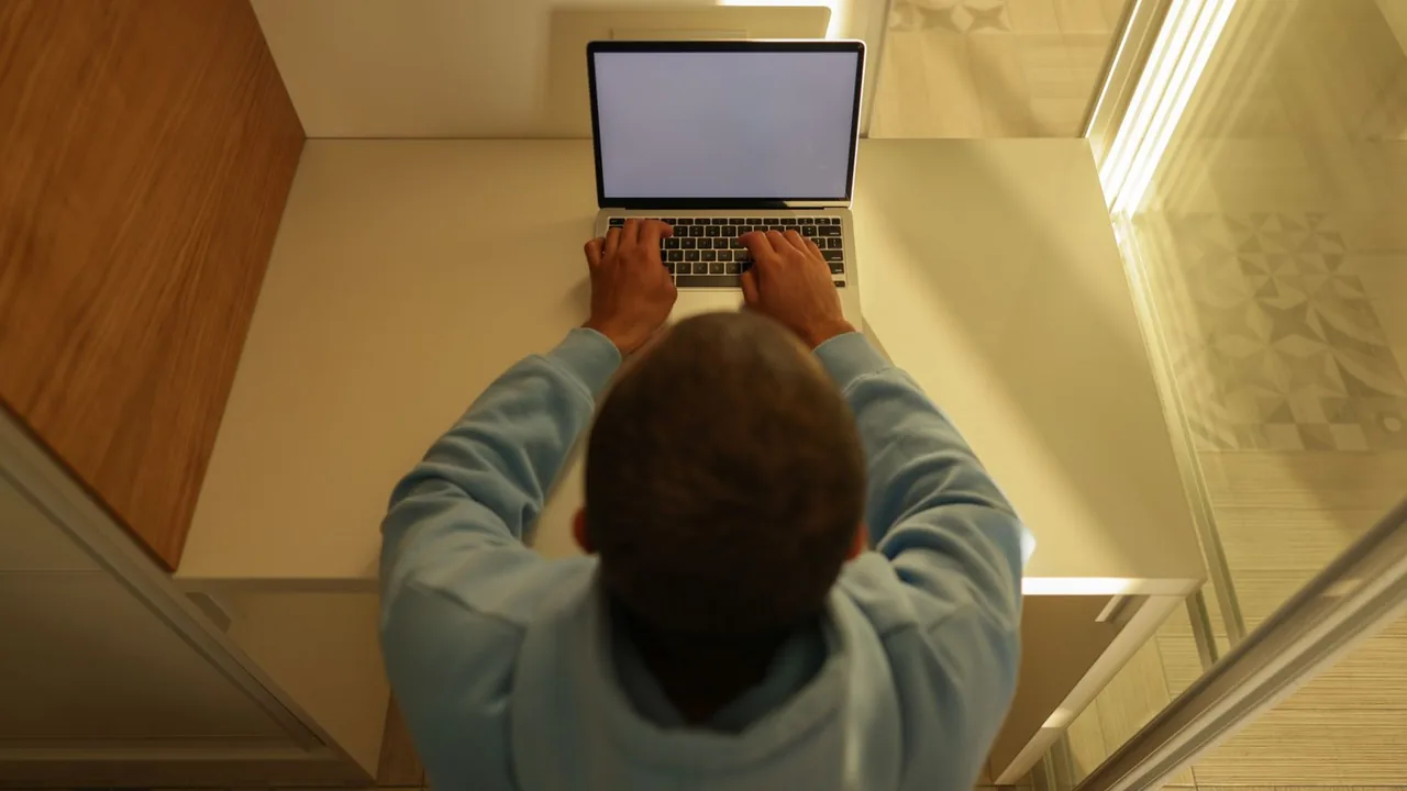 Vue de dessus d'un homme tapant sur un ordinateur portable dans un coin de bureau aux tons chauds