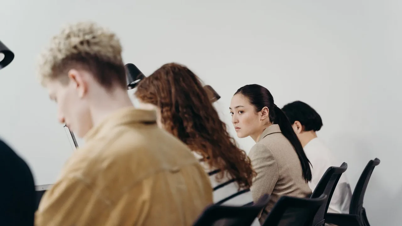 Quatre collègues assis en rang, vus de profil devant un mur blanc, la plupart penchés sur leur travail