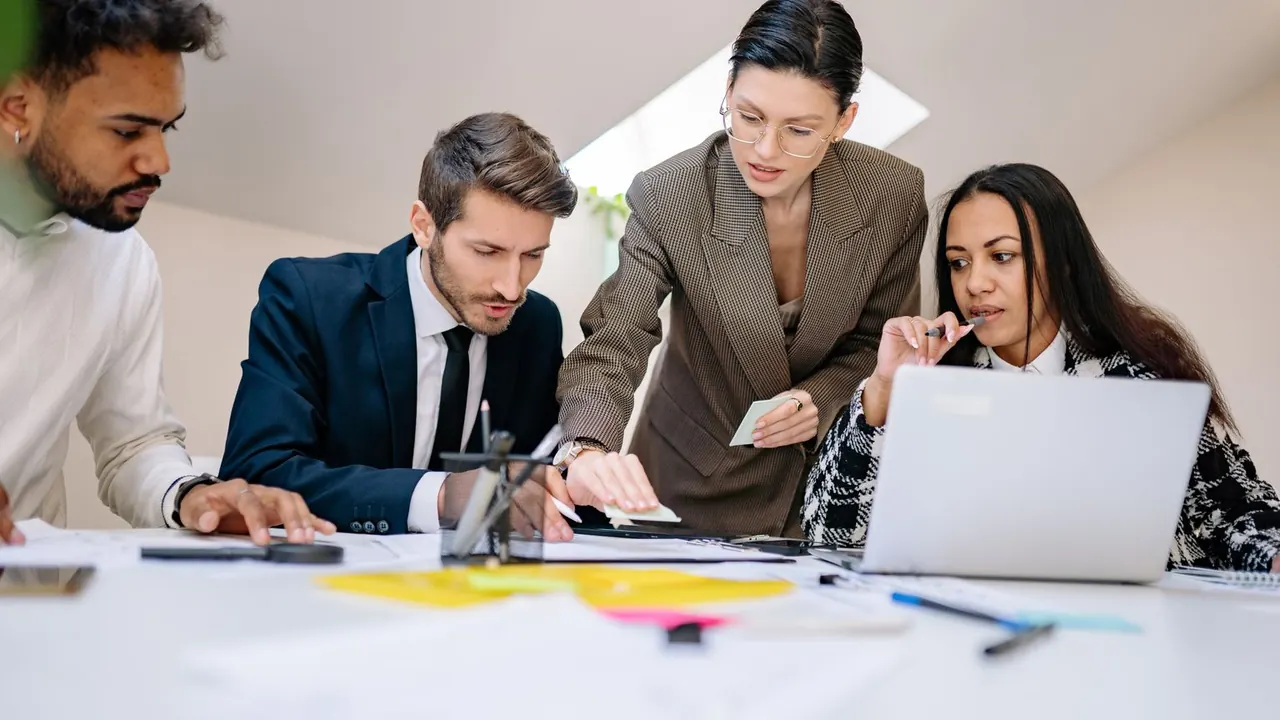 Équipe réunie autour d'une table de travail avec documents et ordinateur portable