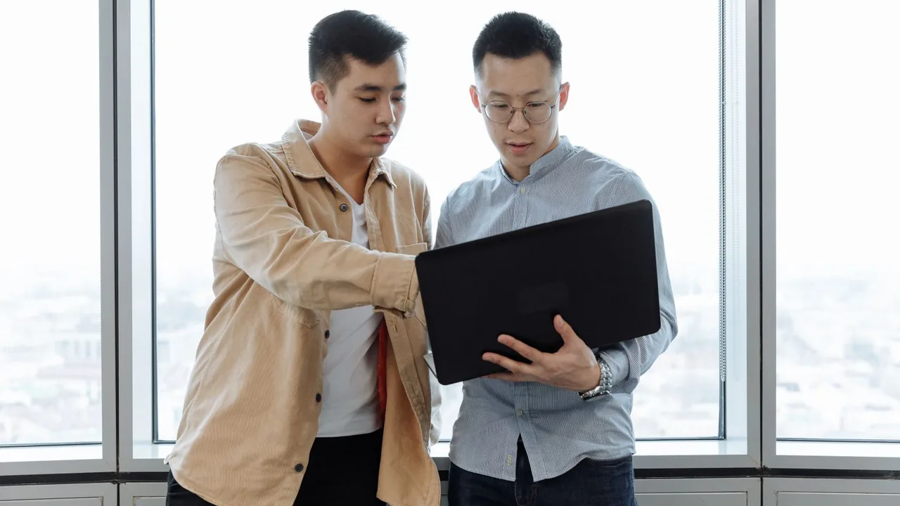 Deux collègues regardent ensemble un ordinateur portable près d'une grande fenêtre