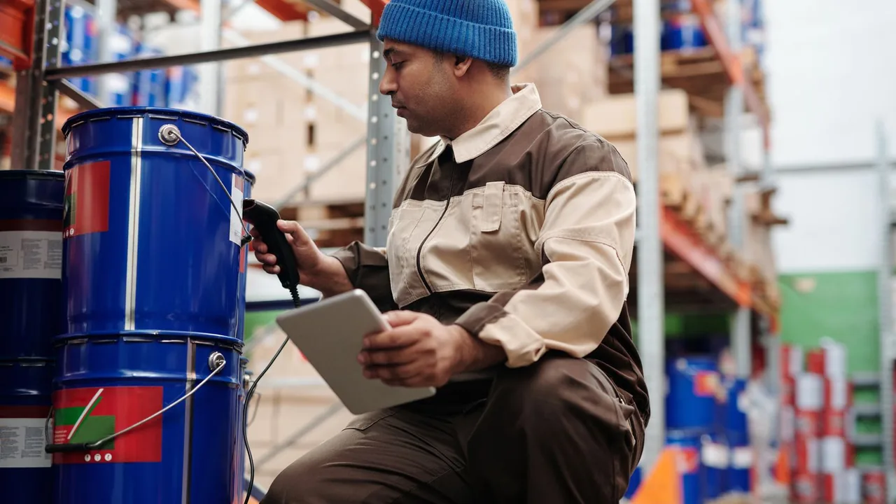 Un employé d'entrepôt scanne l'inventaire avec un lecteur et une tablette devant des fûts