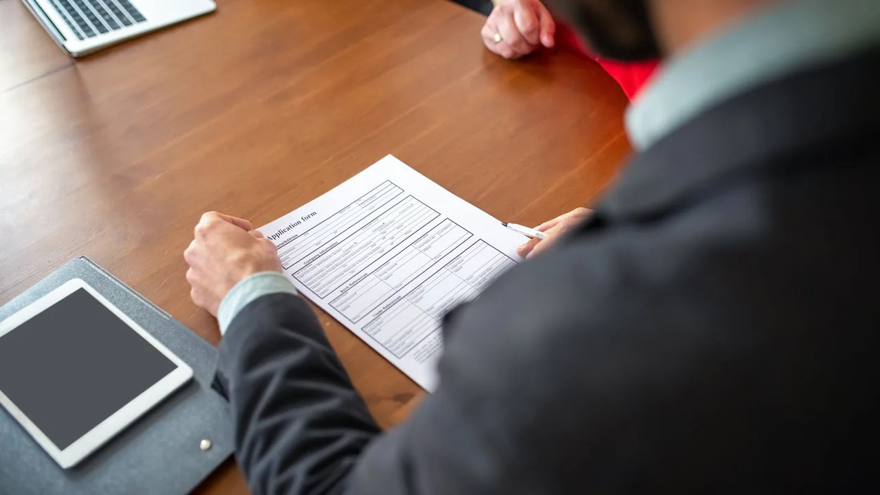Une personne examine un formulaire de candidature posé sur une table, à côté d'une tablette.