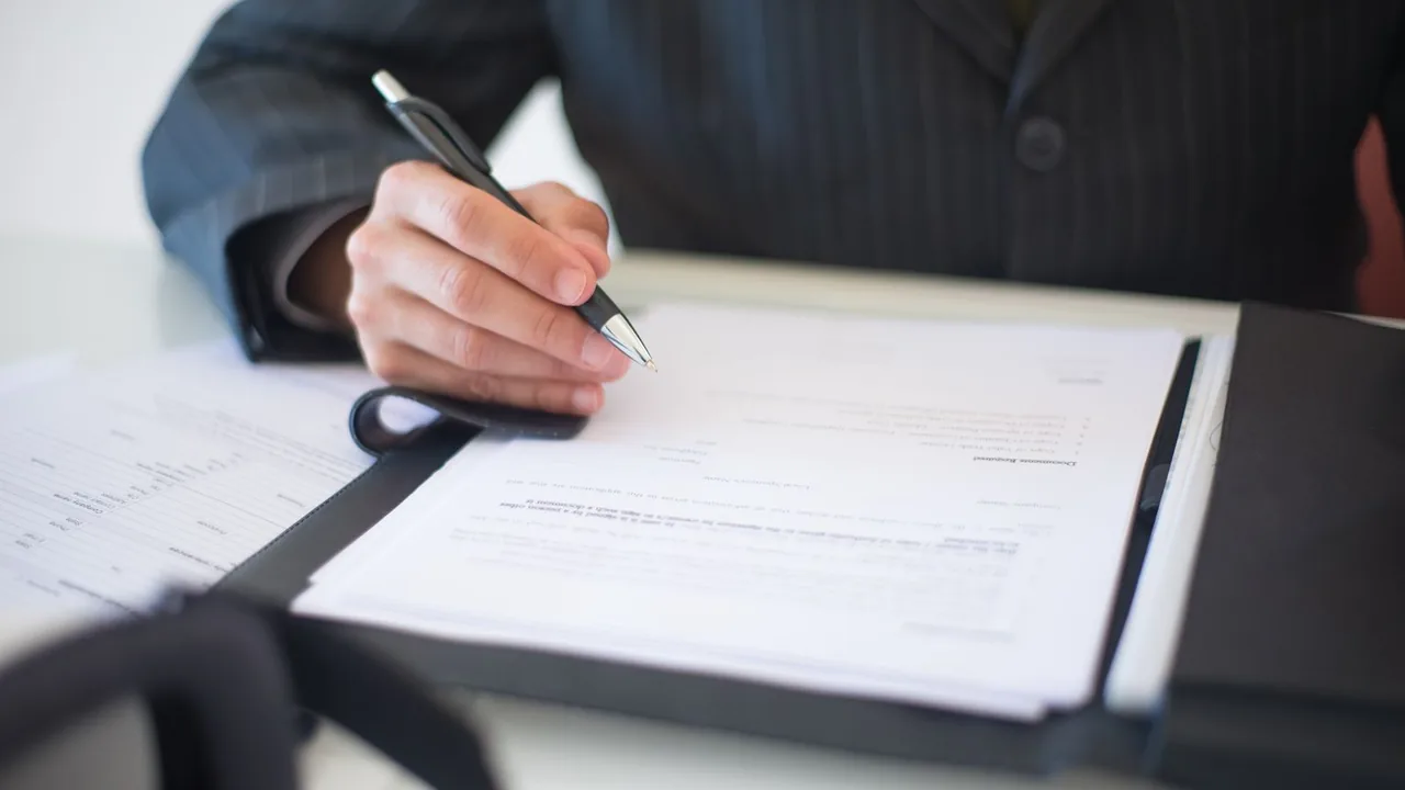 Une main signe un document posé dans un porte-bloc.