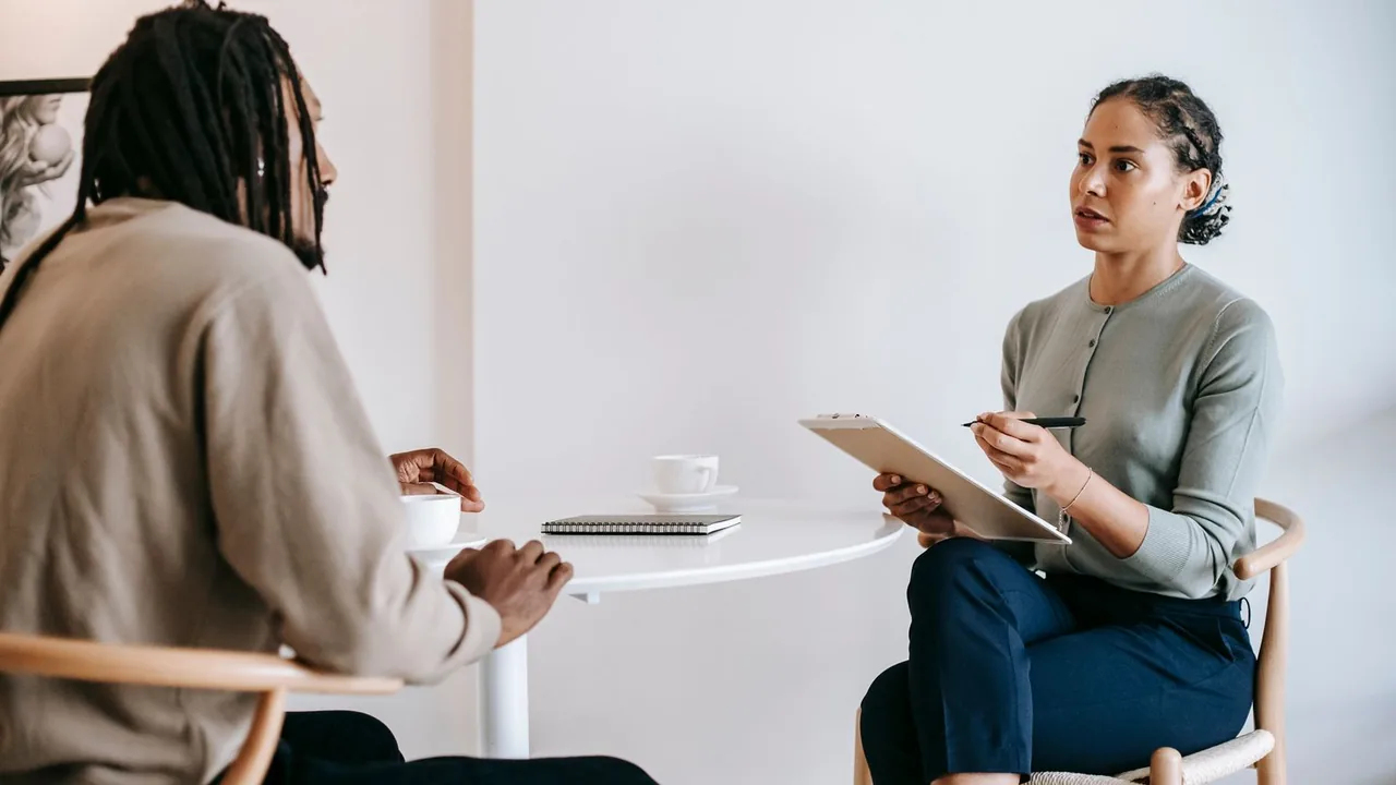 Un homme et une femme échangent à une table ronde, la femme prend des notes sur un bloc