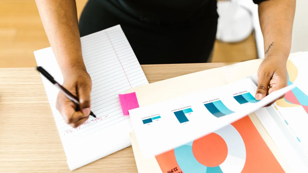 Mains qui prennent des notes à côté de rapports imprimés aux graphiques colorés posés sur un bureau