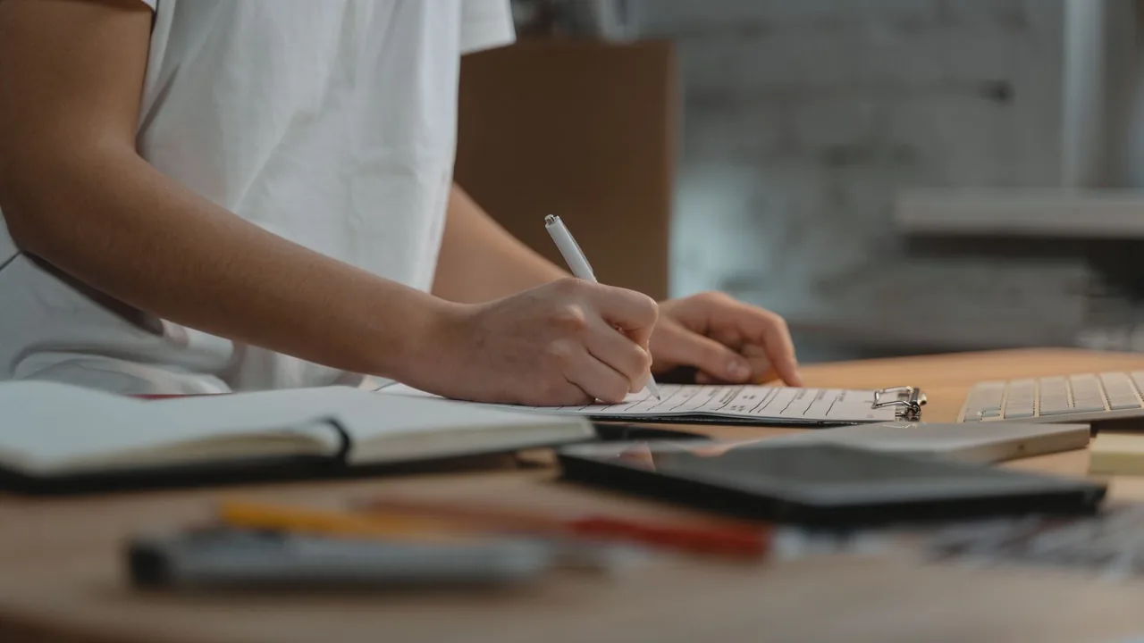 Gros plan d'une main qui écrit sur un bloc-notes posé sur un bureau
