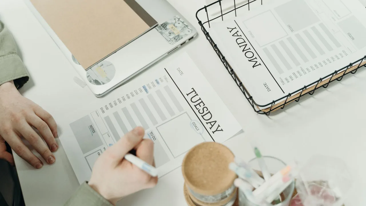 Vue du dessus d'un bureau avec un planning hebdomadaire imprimé, une main qui écrit au feutre