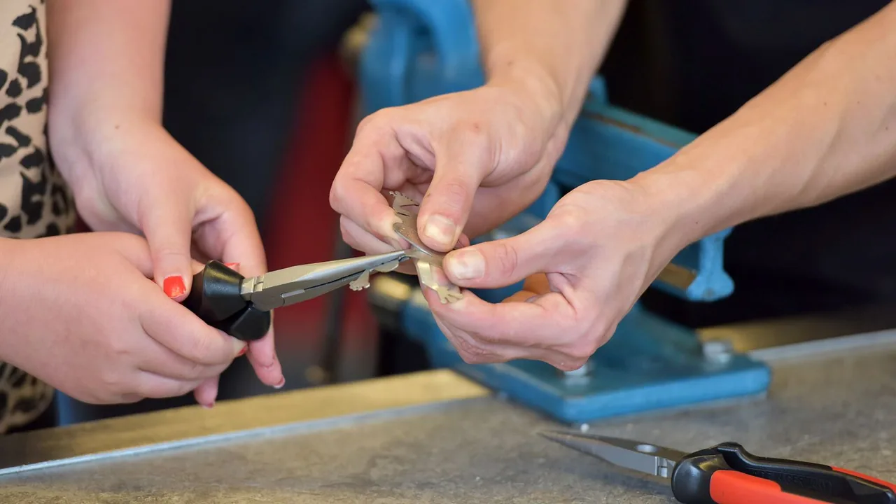 Deux paires de mains assemblent une petite pièce métallique avec une pince, devant un étau bleu